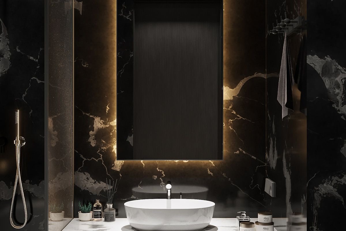 Baño con paredes de mármol oscuro, espejo retroiluminado y lavabo blanco