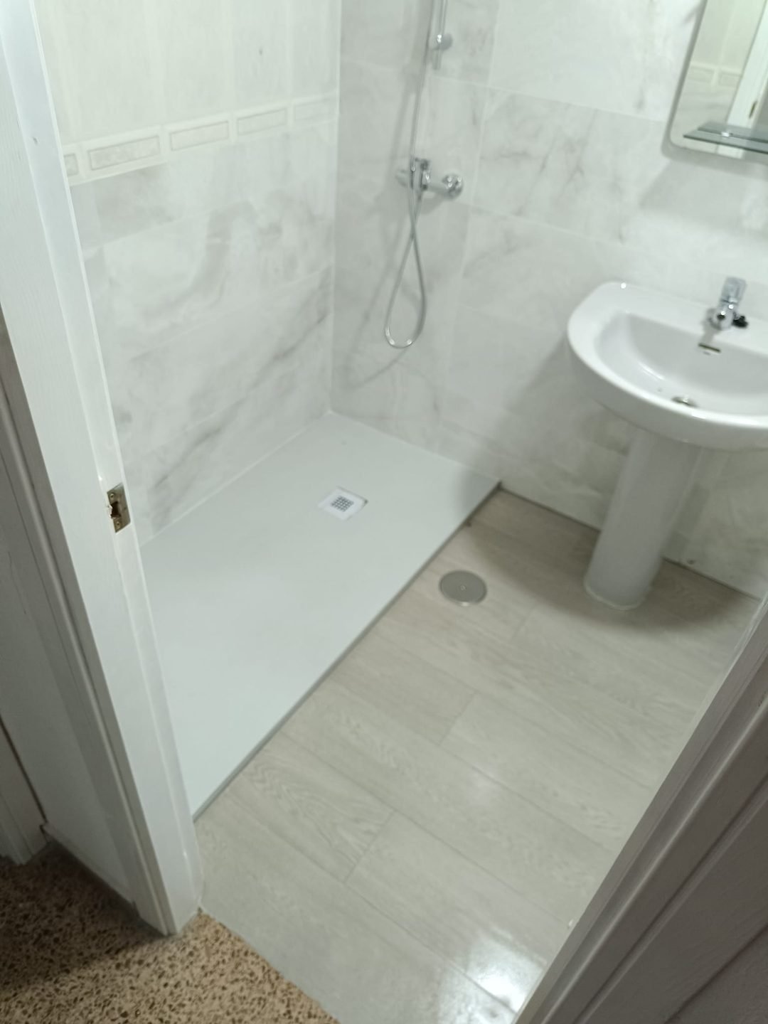 Baño con plato de ducha blanco a ras de suelo y revestimiento de mármol