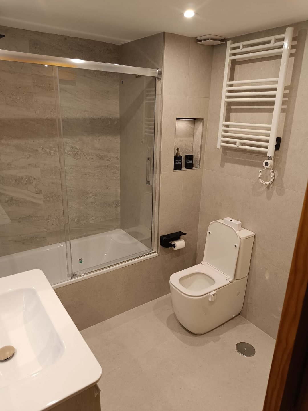 The same bathroom finished, with the bath closed off by a sliding glass screen, a niche in the wall, a new WC and a towel radiator
