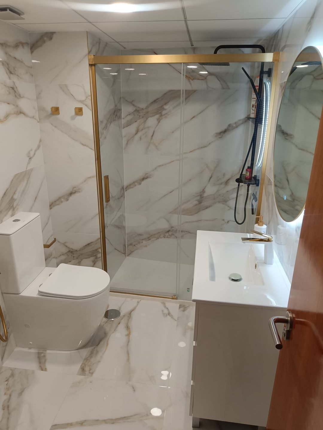 The finished bathroom with the shower closed off by a gold framed screen, the WC and the vanity unit