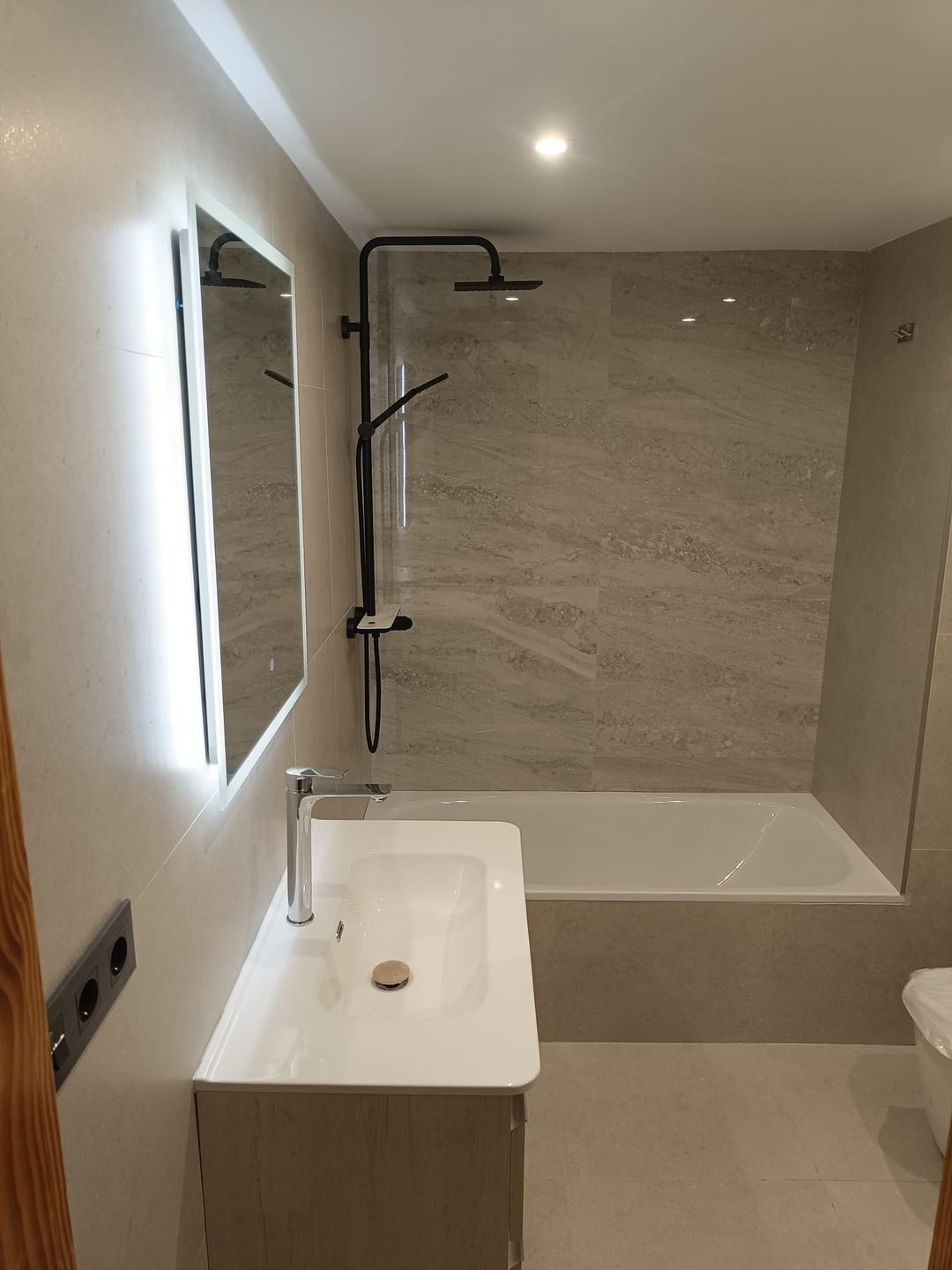 The finished bathroom seen from the door, with the black column over the bath