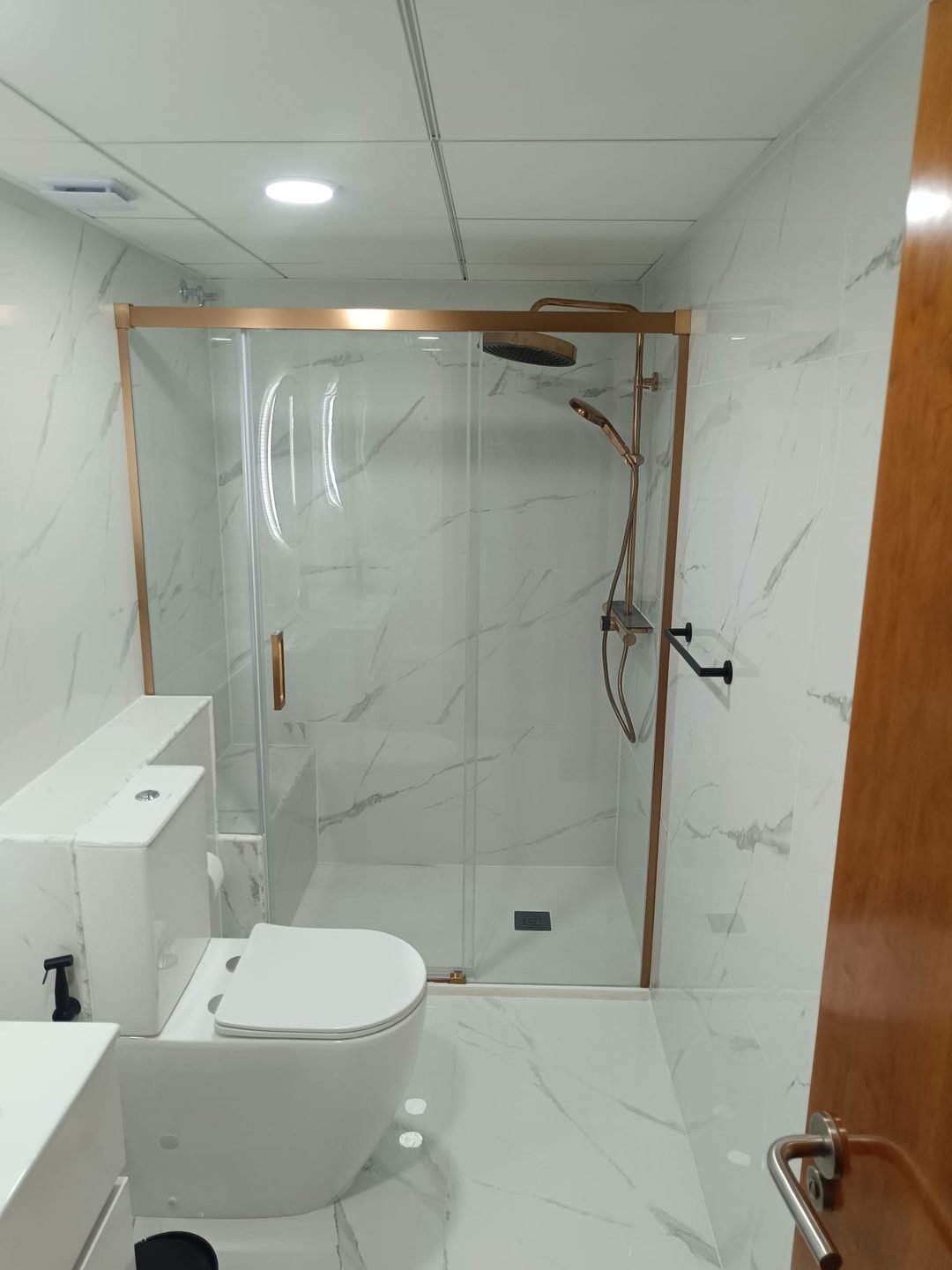 El mismo baño terminado, con la ducha a ras de suelo y mampara corredera de perfil oro rosa