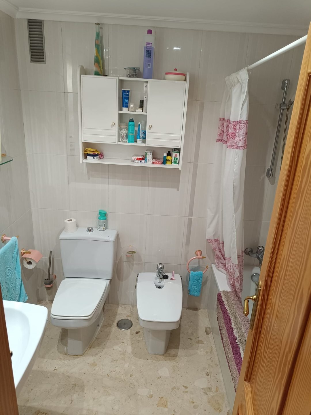 Baño antiguo con bañera, cortina de flores, bidé y mueble alto de pared