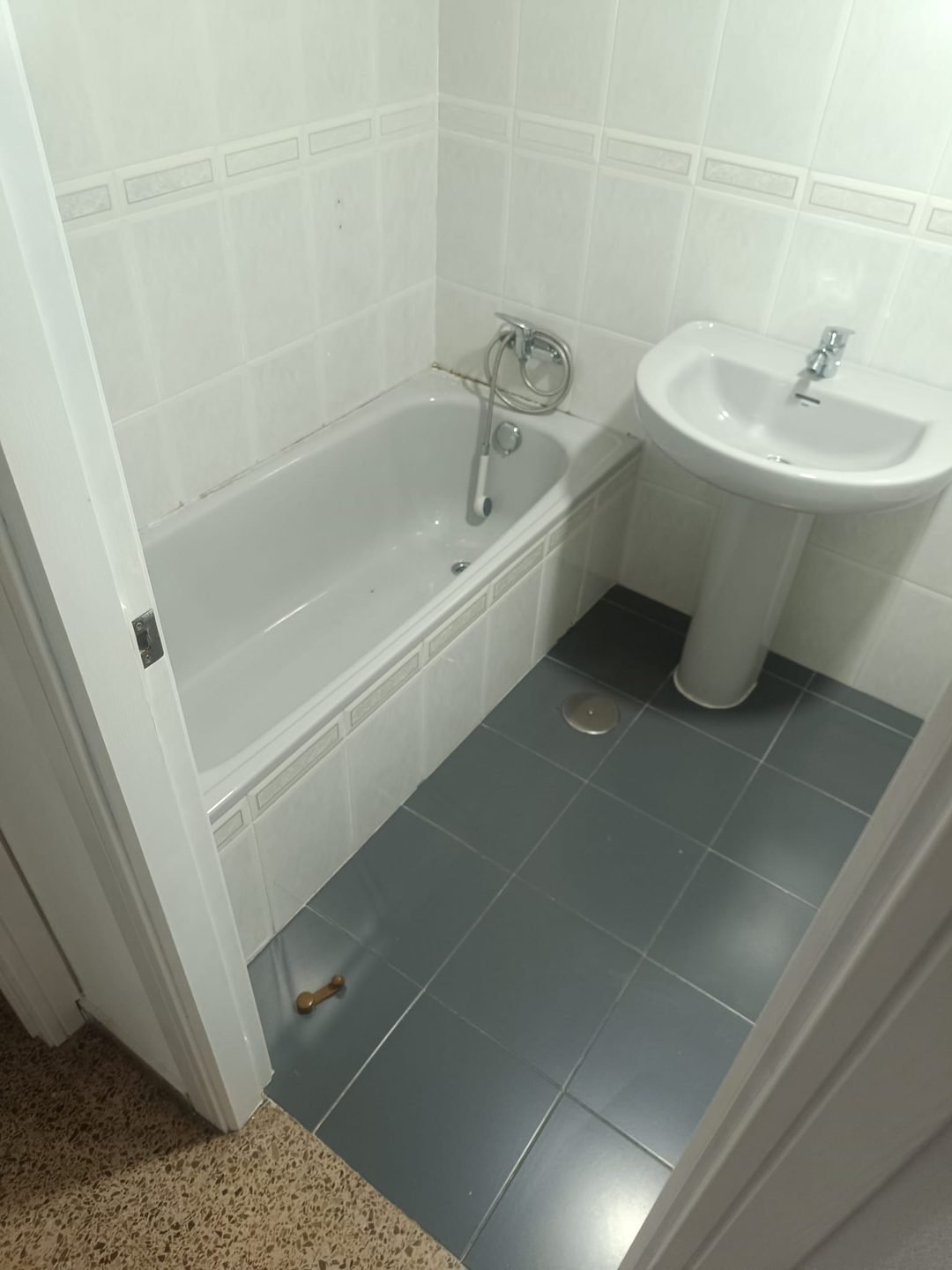 Baño antiguo con bañera empotrada, alicatado blanco con cenefa y lavabo de pie