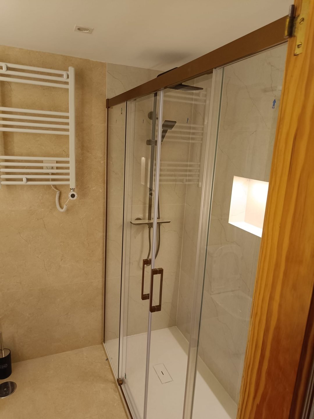 Ducha con mampara corredera de tiradores en bronce y hornacina embebida en el paño alicatado