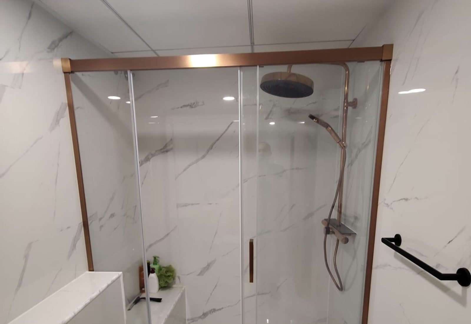 Built-in shower with a rose gold framed screen, tiled bench and matching column in a bathroom handed over in Alicante