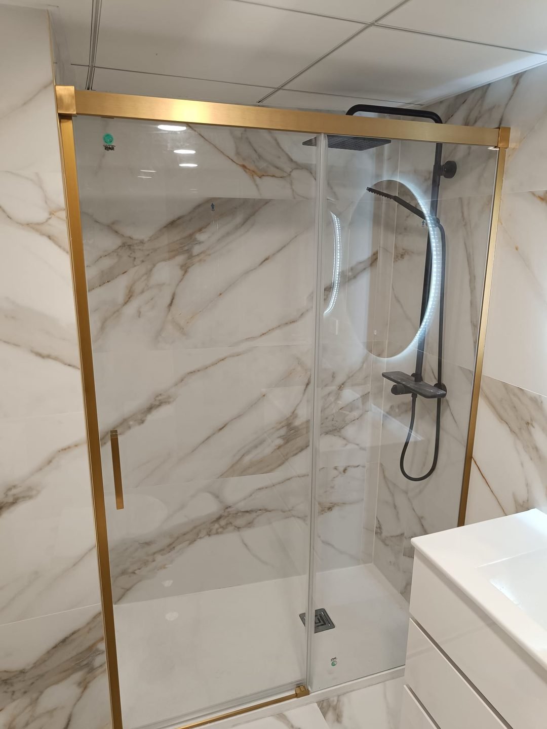 Mampara corredera de perfil dorado sobre porcelánico veteado en un baño entregado en Alicante