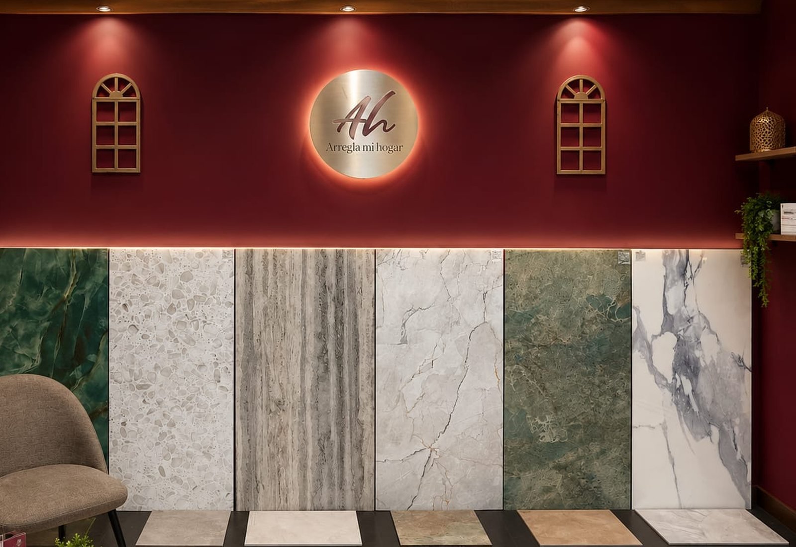 Exposición de Arregla mi hogar en Alicante: pared burdeos con el rótulo de la empresa y muestras de porcelánico y mármol a tamaño real