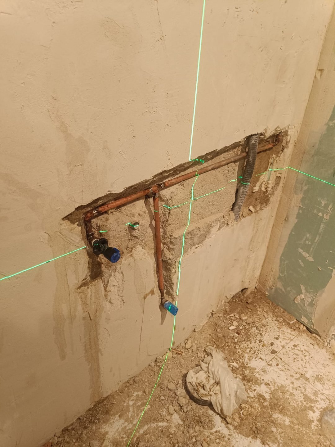 Plumbing installation exposed on the stripped wall, with a laser level marking the heights