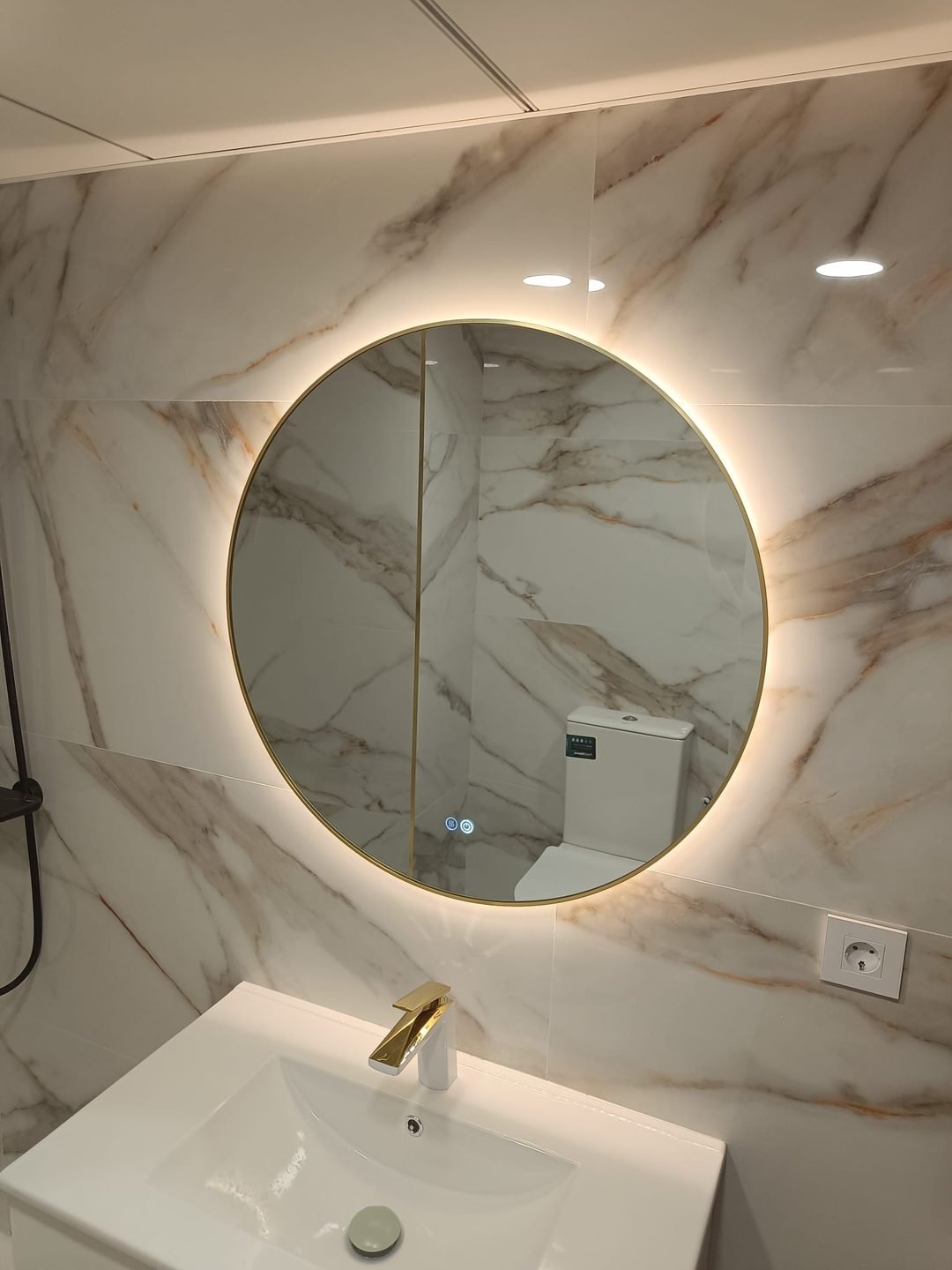 Basin with gold taps under a round backlit mirror