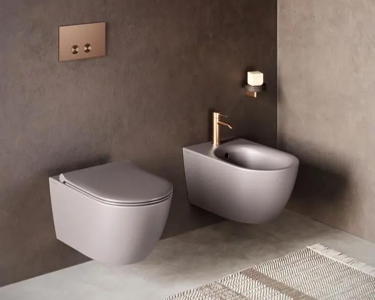 Sanitario y bidet modernos con acabado gris y detalles en cobre, instalados en baño contemporáneo de Arreglamihogar.